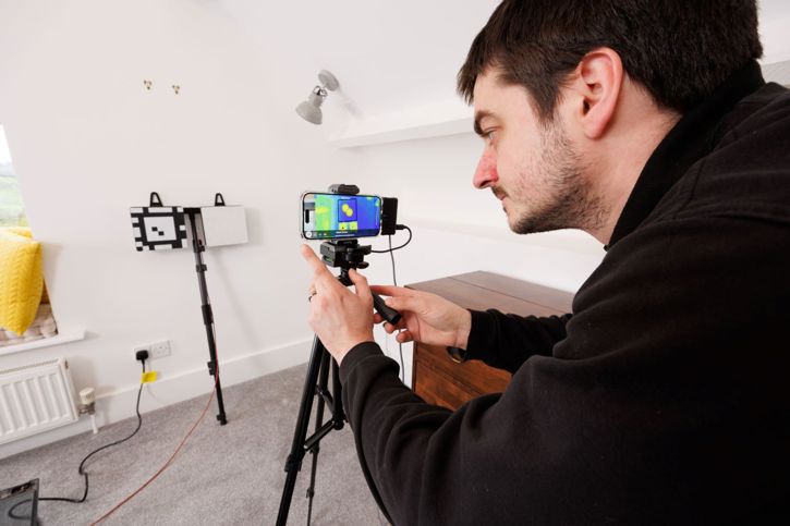 man looking at an iphone with a flir one thermal camera attached studying the thermal pattern of a wall