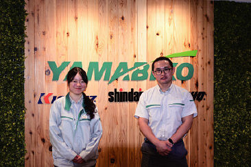 a woman on the left and man on the right standing in front of a sign that says yamabiko