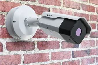 a flir fcb camera against a brick wall