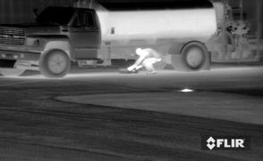 a thermal image of a person sneaking around a parking lot
