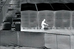 a thermal image of a person sneaking around a parking lot